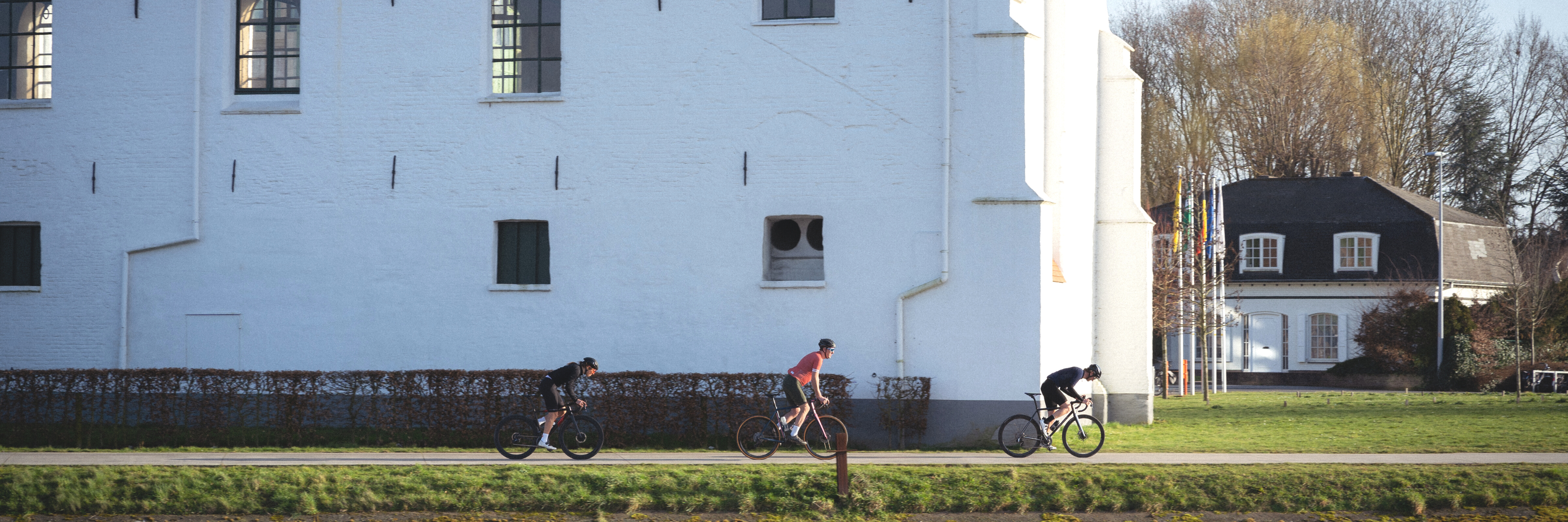 3 fietsers fietsen op een rijtje voorbij de nieuwe wielerhub in oudenaarde