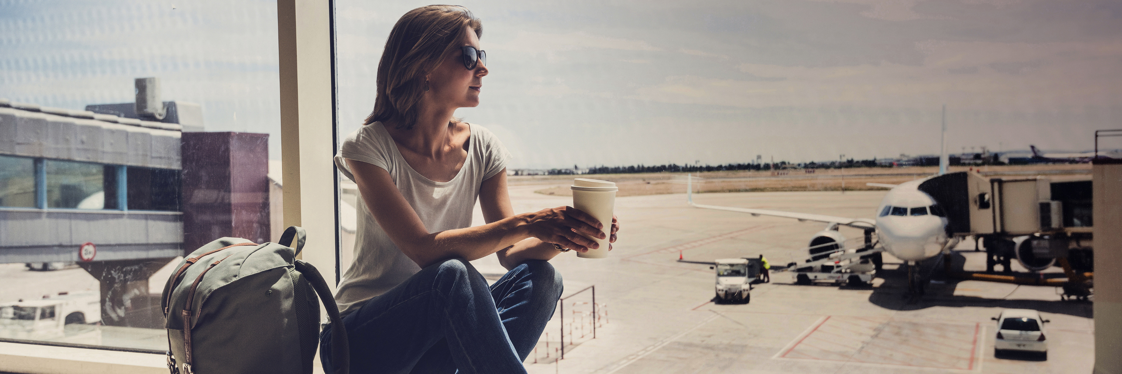 Een vrouw met rugzak drinkt koffie op het vliegveld