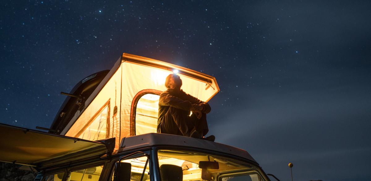 man zit op dak tent op auto te staren naar sterrenhemel